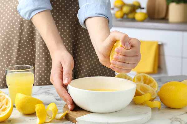 Woman squeezing lemon juice into bowl at marble table, closeup