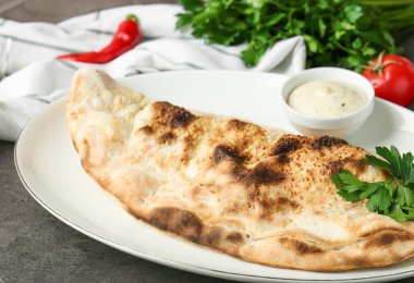 Gri masadaki sosla servis edilen leziz calzone, yakın plan.