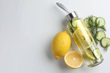 Şişe içinde limon suyu, biberiye, taze meyve ve beyaz arka planda salatalık dilimleri, düz yatak. Metin için boşluk