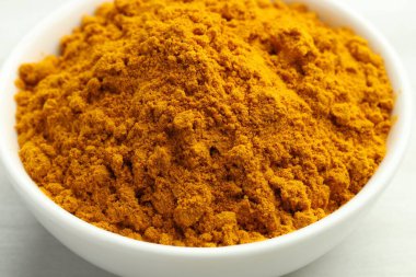 Beyaz masadaki kasede zerdeçal tozu, yakın plan.