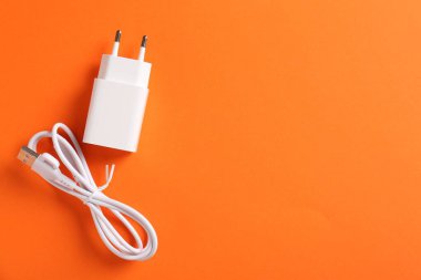 USB güç adaptörü ve turuncu arka planda şarj kablosu, düz konum. Metin için boşluk