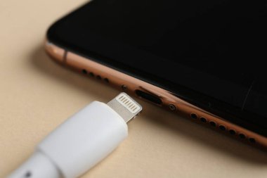 Bej arka planda USB şarj kablosu ve akıllı telefon, yakın plan