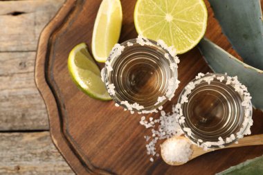 Tuzlu tekila shot 'ları, limon dilimleri ve ahşap masa üzerinde agave yaprakları.