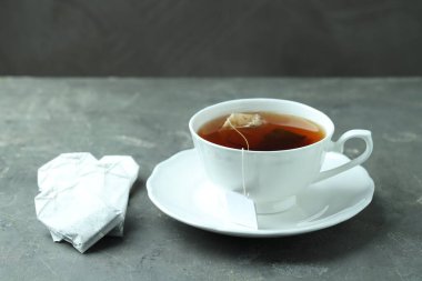 Gri dokulu masada sıcak içecekle çay poşeti ve fincan.