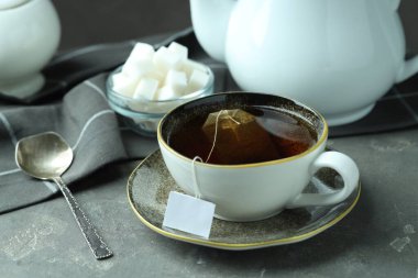 Çay poşeti sıcak içecek, çaydanlık, şeker küpleri ve gri desenli masada kaşık.