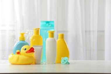 Bebek kozmetik ürünleri, emzik, plastik ördekler ve açık tahta masa üzerinde uçan baloncuklar. Metin için boşluk