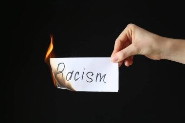 Woman holding burning card with word Racism on black background, closeup clipart