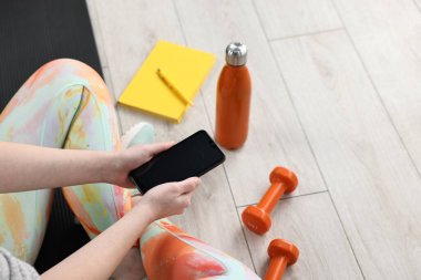 Akıllı telefonu olan bir kadın, spor aletleri ve kapalı bir yerde planlamacı, yakın plan. Metin için boşluk