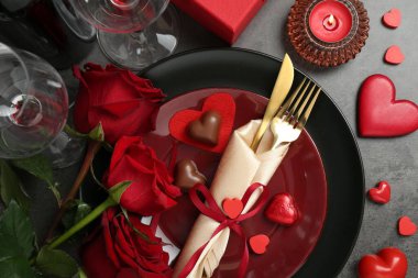 Sevgililer Günü için romantik bir yer. Masa takımı, çatal bıçak takımı, şekerler, güller ve dekoratif kalpler gri desenli masa, düz yatak