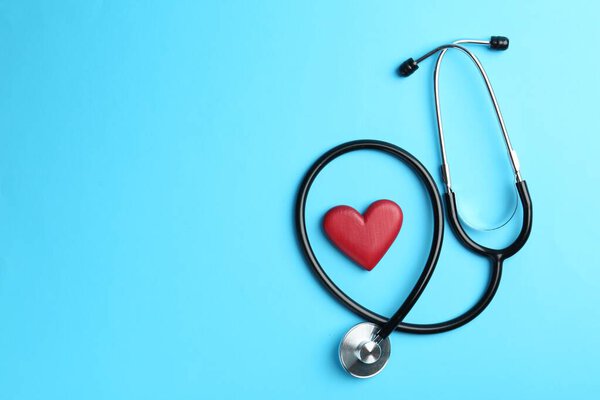 Cardiology. Stethoscope and red decorative heart on light blue background, flat lay. Space for text