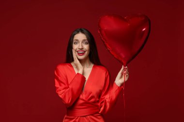 Sevgililer Günün kutlu olsun. Kırmızı arka planda kalp şeklinde balonu olan güzel bir kadın.