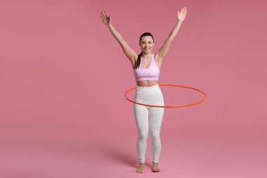 Gülümseyen kadın eğitimi pembe arka planda hula hoop ile
