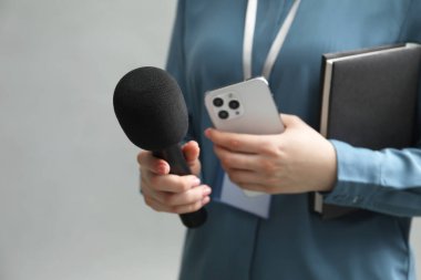 Mikrofonu, akıllı telefonu ve gri arka planda defteri olan bir gazeteci, yakın plan. Metin için boşluk