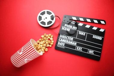 Film alkışı, tatlı patlamış mısır ve kırmızı arka planda film makarası, düz konum