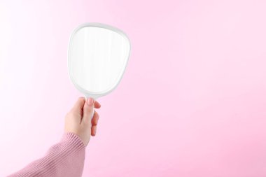 Pembe arka planda el yapımı aynayı tutan kadın, yakın plan. Metin için boşluk
