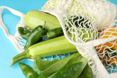 Açık mavi arka planda ürünleri olan ağ torbası, yakın plan. Çevre dostu yaşam tarzı