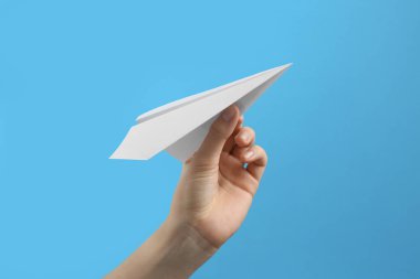 Açık mavi arka planda beyaz kağıt uçaklı kadın, yakın plan.