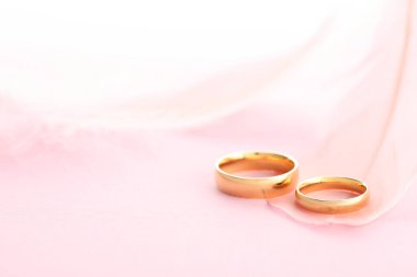 Pembe arka planda güzel altın alyanslar ve tüy, yakın plan. Metin için boşluk