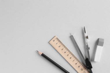 Cetvel, kalem, silgi ve pusula açık gri arka planda, düz yerde. Metin için boşluk