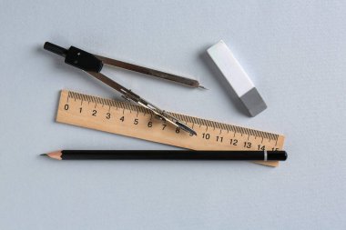 Açık gri arkaplanda cetvel, kalem, silgi ve pusula, düz konum