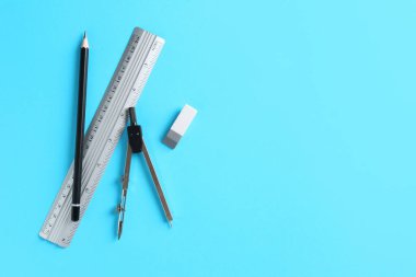 Cetvel, kalem, silgi ve pusula açık mavi arka planda, düz yerde. Metin için boşluk