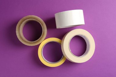 Mor arka planda farklı yapışkan bantların ruloları, düz yatış