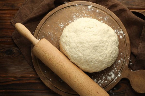 Fresh dough and rolling pin on wooden table, top view