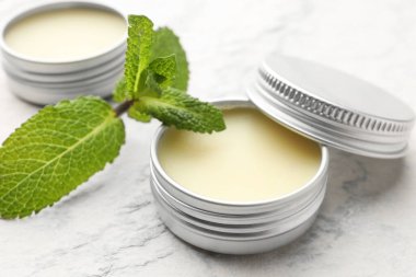 Mint lip balms and green leaves on beige textured table, closeup. Cosmetic product clipart