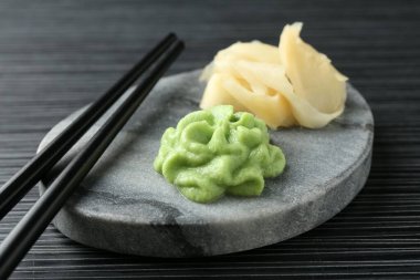 Siyah desenli masa üzerinde sıcak wasabi macunu, zencefil ve çubuk bulunan mermer tahta, yakın plan.