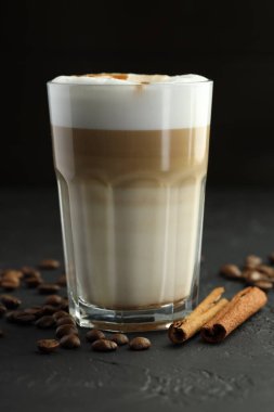 Bardakta latte macchiato, siyah masada kahve çekirdekleri ve tarçın, yakın plan.
