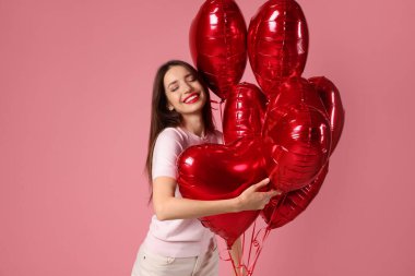 Sevgililer Günün kutlu olsun. Pembe arka planda kalp şeklinde balonları olan güzel bir kadın.