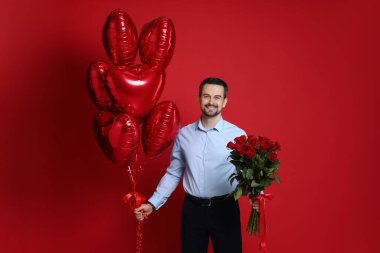 Sevgililer Günün kutlu olsun. Kırmızı arka planda gül buketi ve kalp şeklinde balonları olan yakışıklı bir adam.