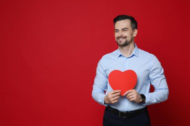 Sevgililer Günün kutlu olsun. Kırmızı arka planda kağıt kalpli yakışıklı bir adam. Metin için boşluk