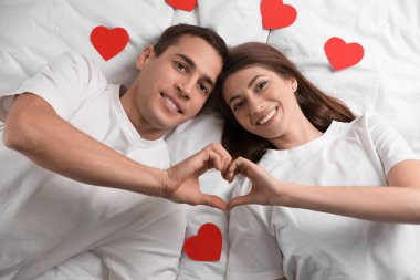Güzel bir çift, elleri yatağın üstünde, güzel bir kalp yapıyor. Sevgililer Günü kutlaması