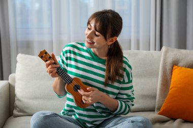 Evdeki kanepede ukulele çalan mutlu kadın.