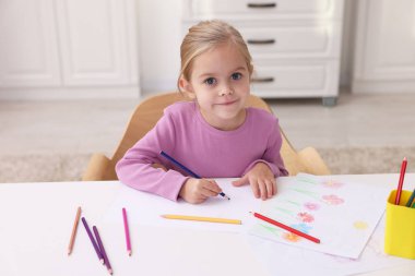Anaokulunda beyaz masada resim çizen tatlı bir kız.