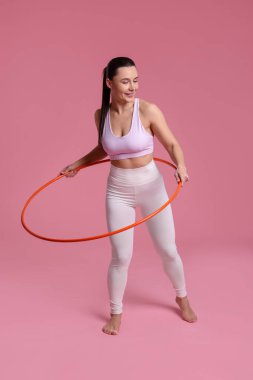 Gülümseyen kadın eğitimi pembe arka planda hula hoop ile