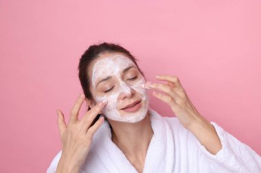 Spa günü. Güzel bir kadın pembe arka planda yüzüne maske takıyor.
