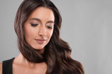 Saç şekillendirme. Gri arka planda dalgalı uzun saçlı güzel bir kadın, yakın plan. Metin için boşluk