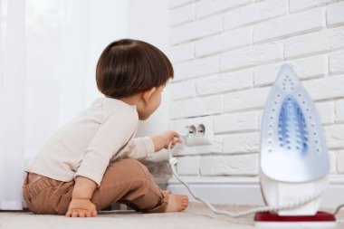 Küçük çocuk evde demir fiş ve elektrik priziyle oynuyor. Çocuk tehlikede.