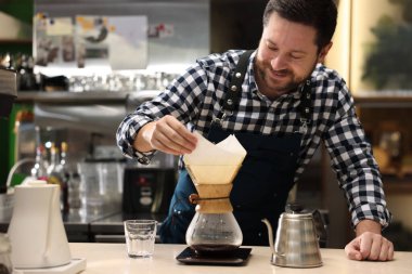 Barista, kafedeki masada cam kahve makinesiyle kahve yapıyor.