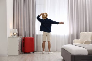 Gezgin ve bavul, otel odasının penceresinin yanında.