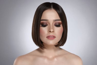 Gri arkaplanda muhteşem düz saçlı ve şık makyajlı güzel bir genç kadının portresi.