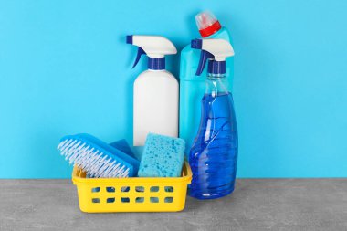 Gri masada açık mavi zemine karşı farklı temizlik ürünleri ve malzemeler