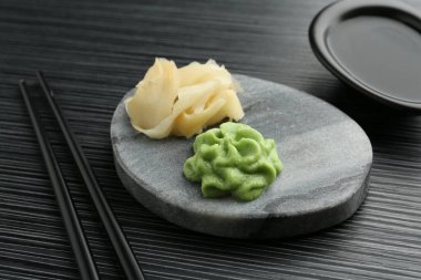 Sıcak wasabi ezmesi, soya sosu, zencefil ve çubuklar siyah desenli masada, yakın plan.