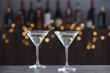 Gri masadaki zeytinli martini kokteyli bulanık arka planda. Bokeh etkisi