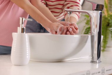 Anne ve kız ellerini lavabonun üstünde yıkıyor, kapalı.
