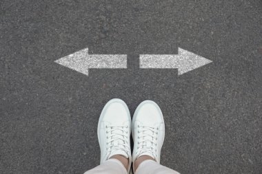 Asfalt yolda beyaz okların yanında duran kadın, yakın plan. Seçim kavramları, karar, farklı yol, alternatif