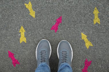 Sarı ve pembe okların yanında duran adam asfalt yolda farklı yönleri işaret ediyor, yakın plan. Seçim, karar, alternatif yol kavramları