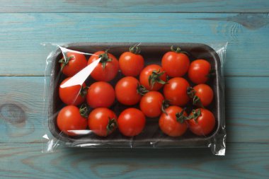 Açık mavi ahşap masa üzerinde bir paket taze domates.